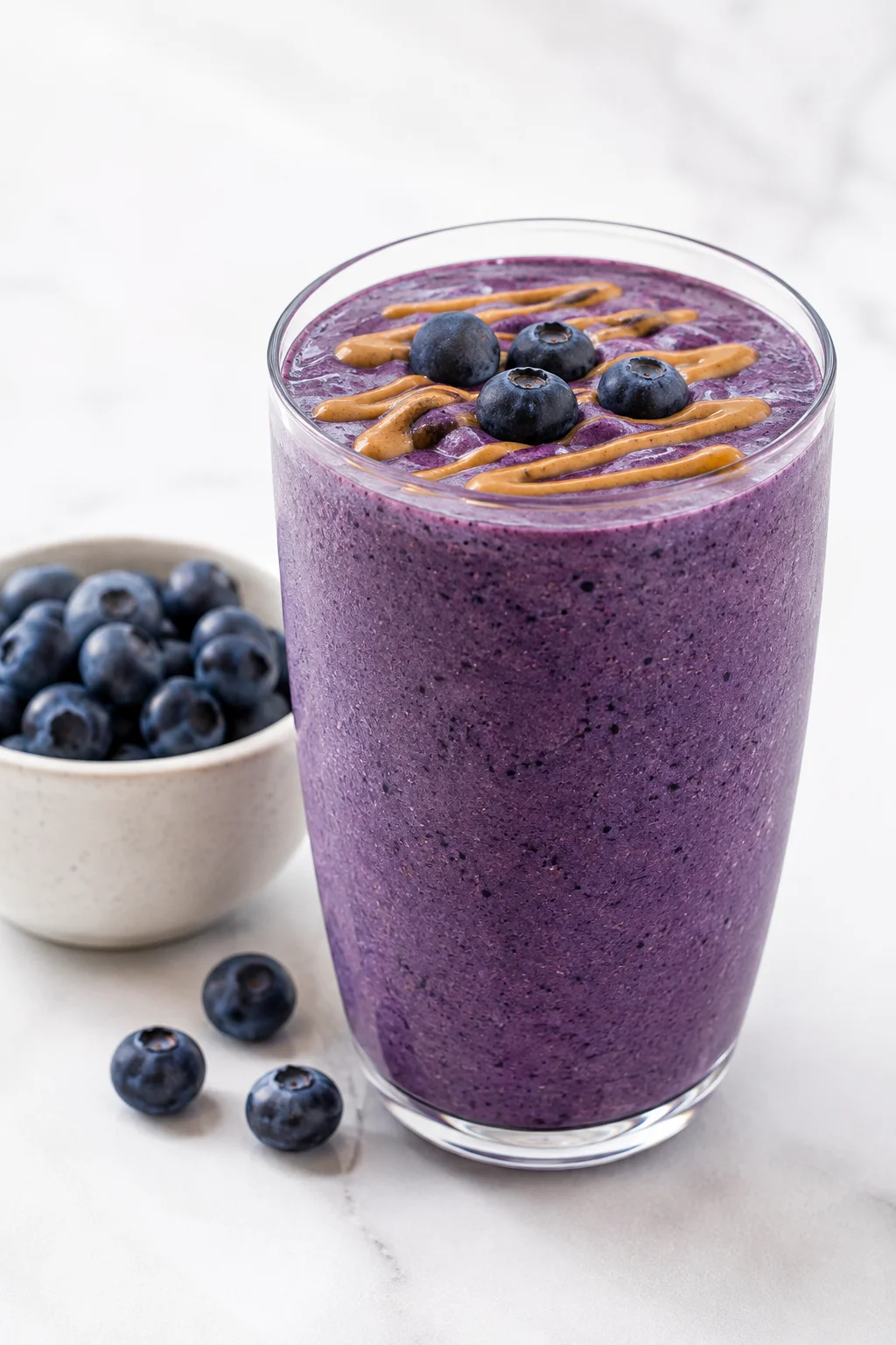 Deep purple blueberry almond protein smoothie topped with fresh blueberries and a drizzle of almond butter